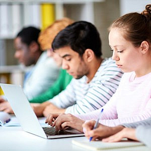 4 people sitting at desk and typing on laptops